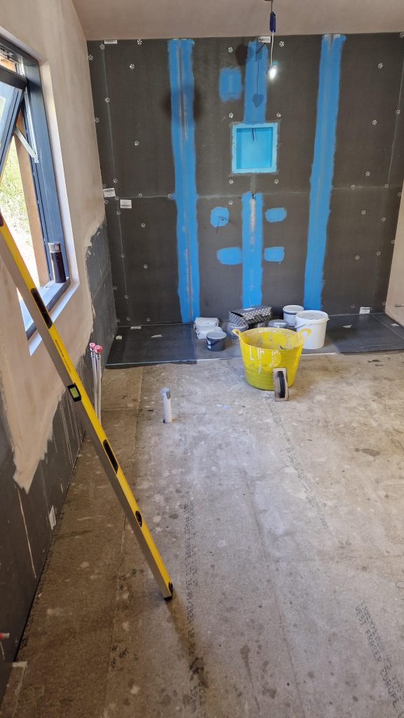 A bathroom stripped back to tile backer board, with the joints and fixings sealed in blue waterproof tanking