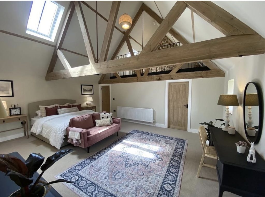 A large bedroom with exposed trusses, freshly painted walls and ceiling, a bed and a sofa on a patterned rug
