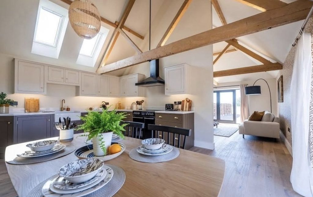 An open plan kitchen and dining room with exposed beams and skylights, painted throughout, with a sitting area beyond