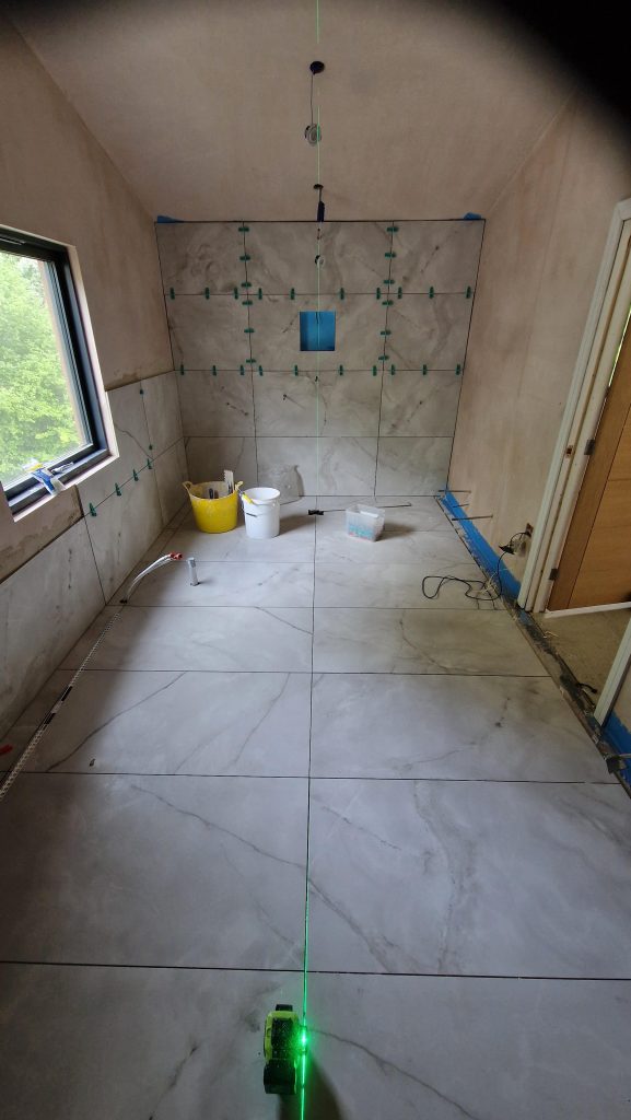 Large marble effect porcelain tiles going up a bathroom wall, held flat with levelling clips and lined up to a laser