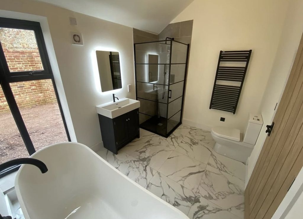 A bathroom floored in large marble effect porcelain, with a black framed shower enclosure, a freestanding bath and a black towel radiator