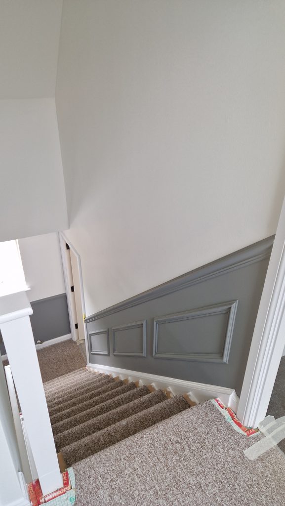 A staircase with grey panelling and a dado rail below pale painted walls