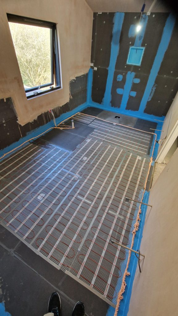 An electric underfloor heating mat laid out across a tanked bathroom floor before tiling